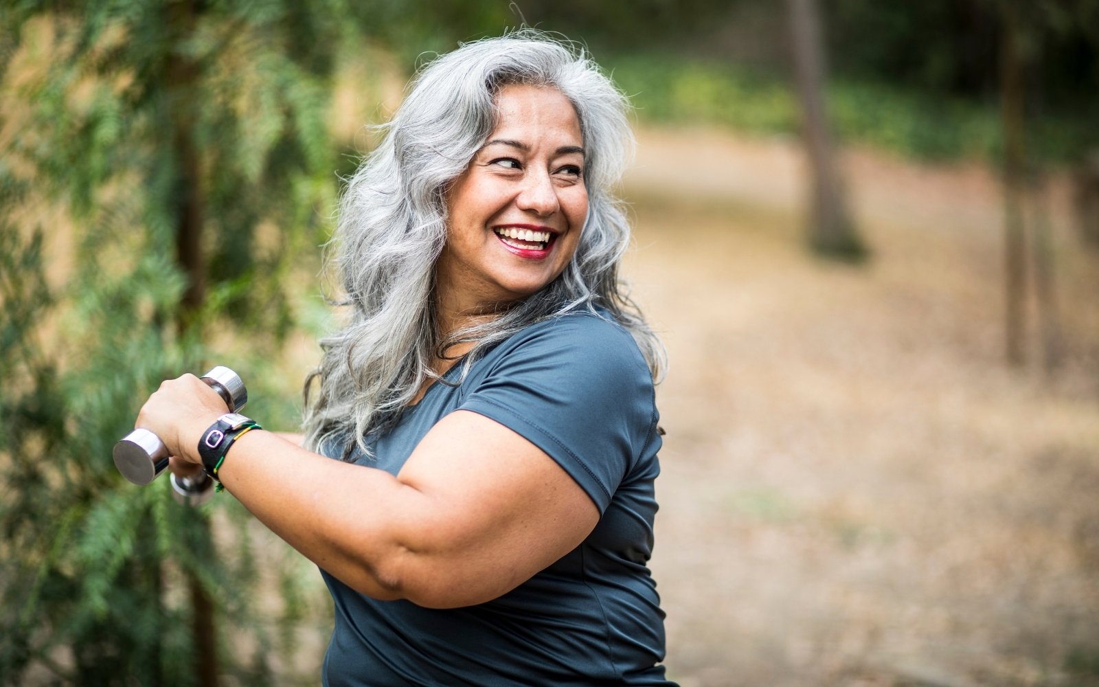 Woman smiling with hand weights outdoors